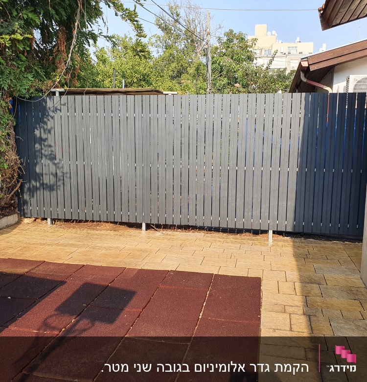 גדר עץ אפורה בחצר עם ריצוף אבן